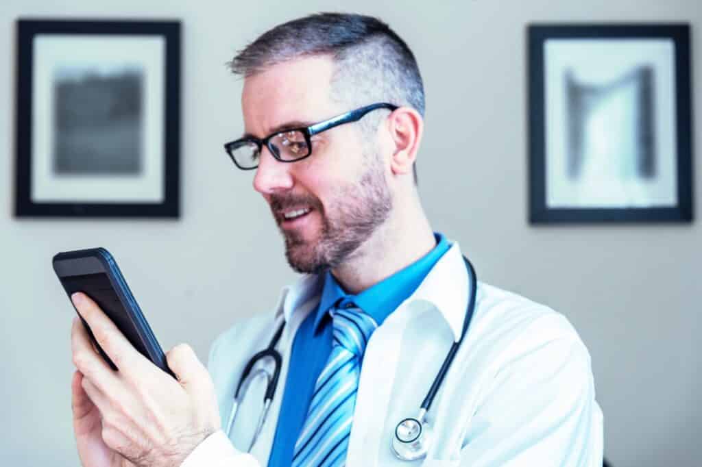 male medical service provider doctor nurse practitioner using a smart phone to video chat conference t20 PQJ3Rr